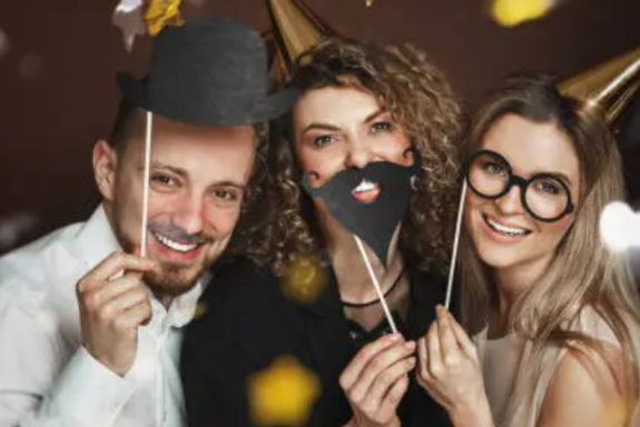 Trois personnes souriantes portant des accessoires festifs et des chapeaux de fête.